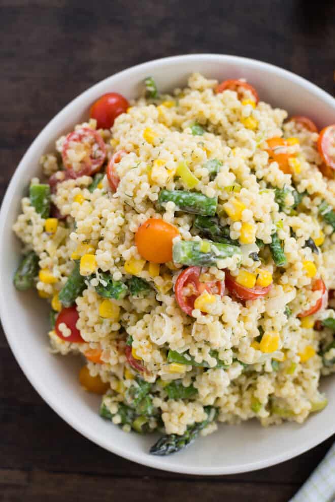 White bowl filled with acini di pepe pasta salad with tomatoes, asparagus and corn.