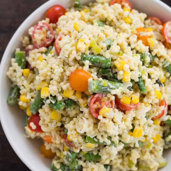 White bowl filled with acini di pepe pasta salad with tomatoes, asparagus and corn.