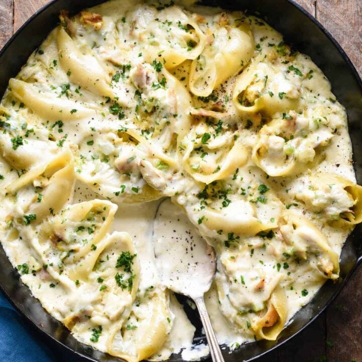 A cast iron skillet filled with chicken alfredo stuffed shells, with a spoon scooping some sauce out.