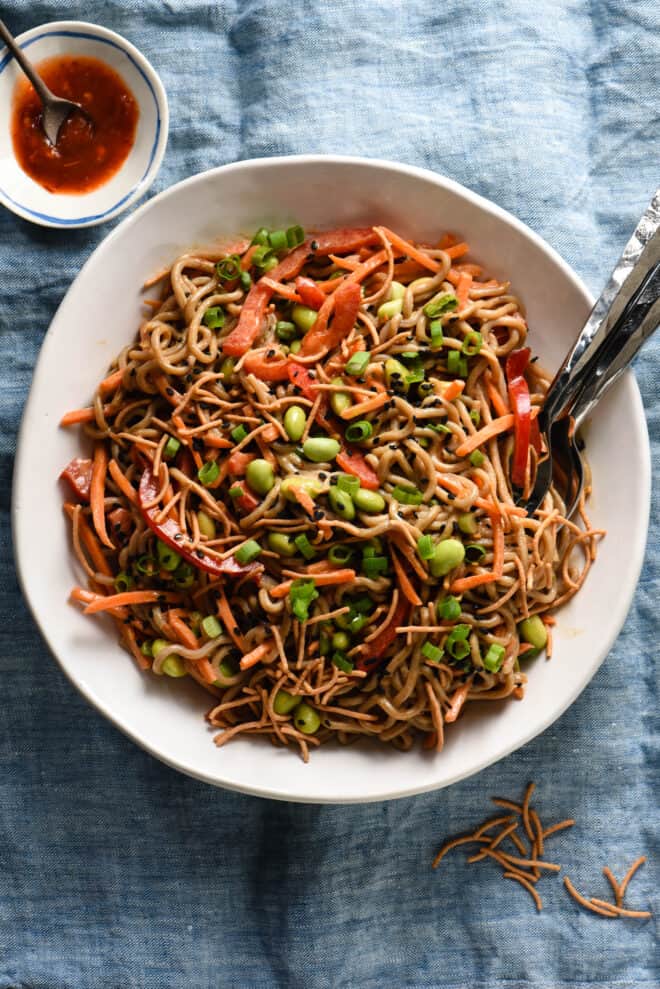 Large white bowl of soba noodles tossed with vegetables, crunchy rice noodles and peanut dressing.