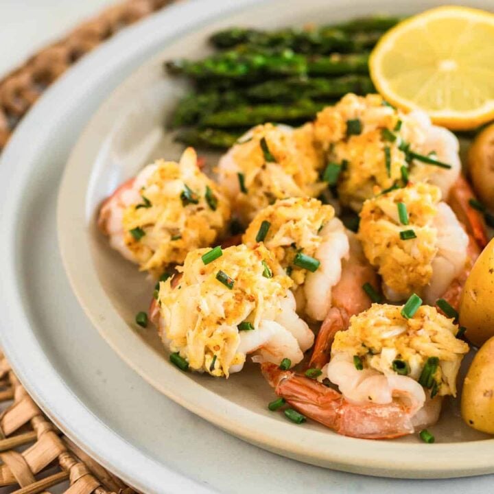 A white plate filled with stuffed shrimp with crab, asparagus, and a lemon half.