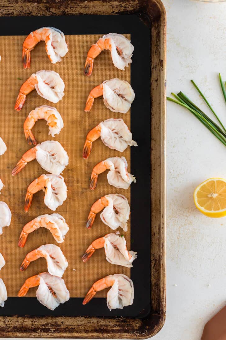 Butterflied prawns arranged in rows on a rimmed baking pan.