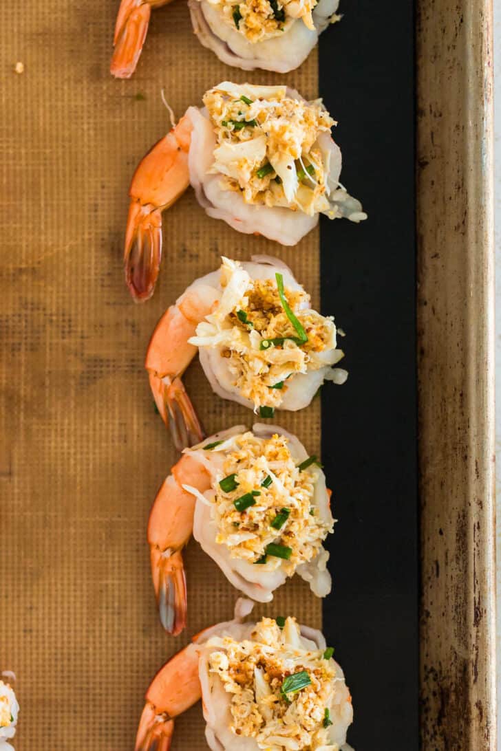 Butterflied shrimp stuffed with a mixture of crab and breadcrumbs on a rimmed baking pan.