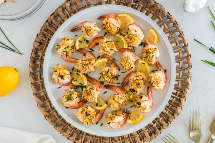 Baked stuff shrimp and lemon wedges on a white plate garnished with chives.