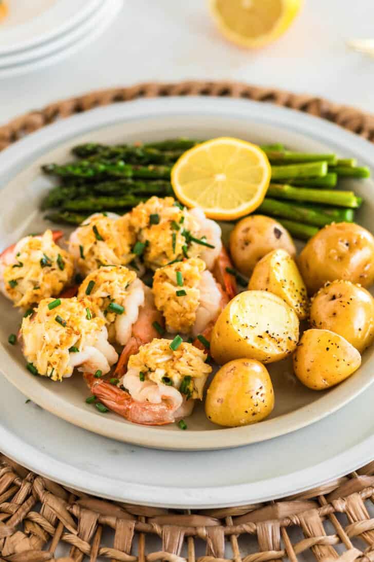 Baked stuffed shrimp, small yellow potatoes, asparagus, and a lemon half on a white plate.