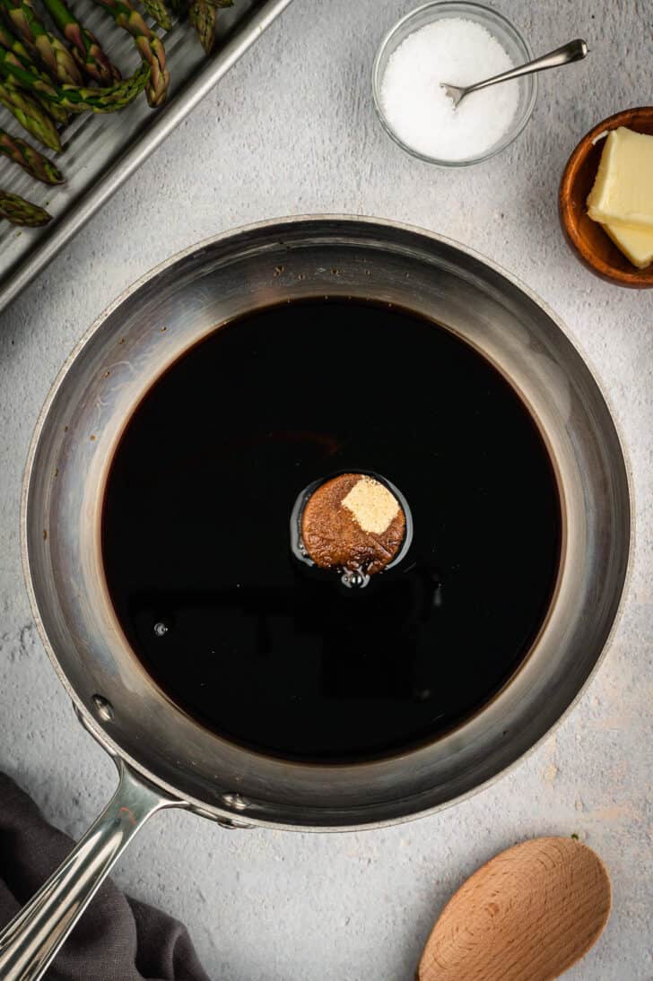 Stainless steel skillet filled with a dark brown liquid and a bit of brown sugar.