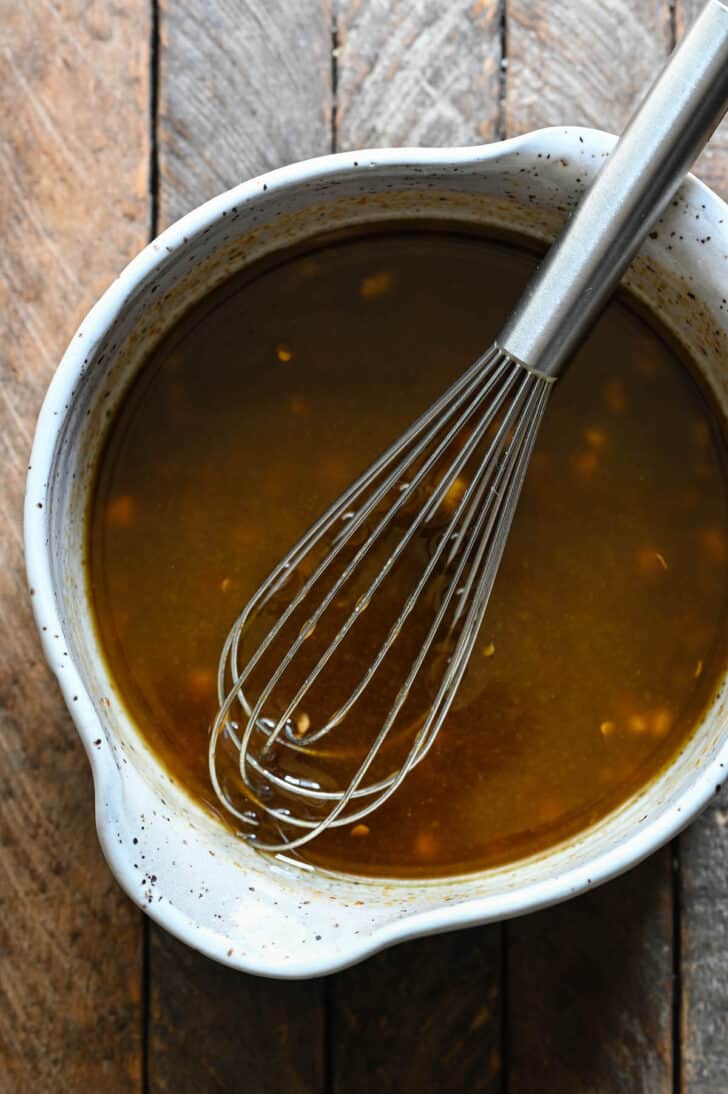 A speckled bowl filled with balsamic vinegar steak marinade, with a metal whisk in it.