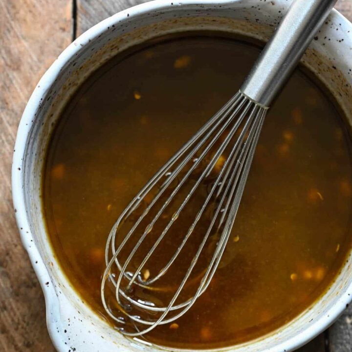 A speckled bowl filled with balsamic steak marinade, with a metal whisk in it.