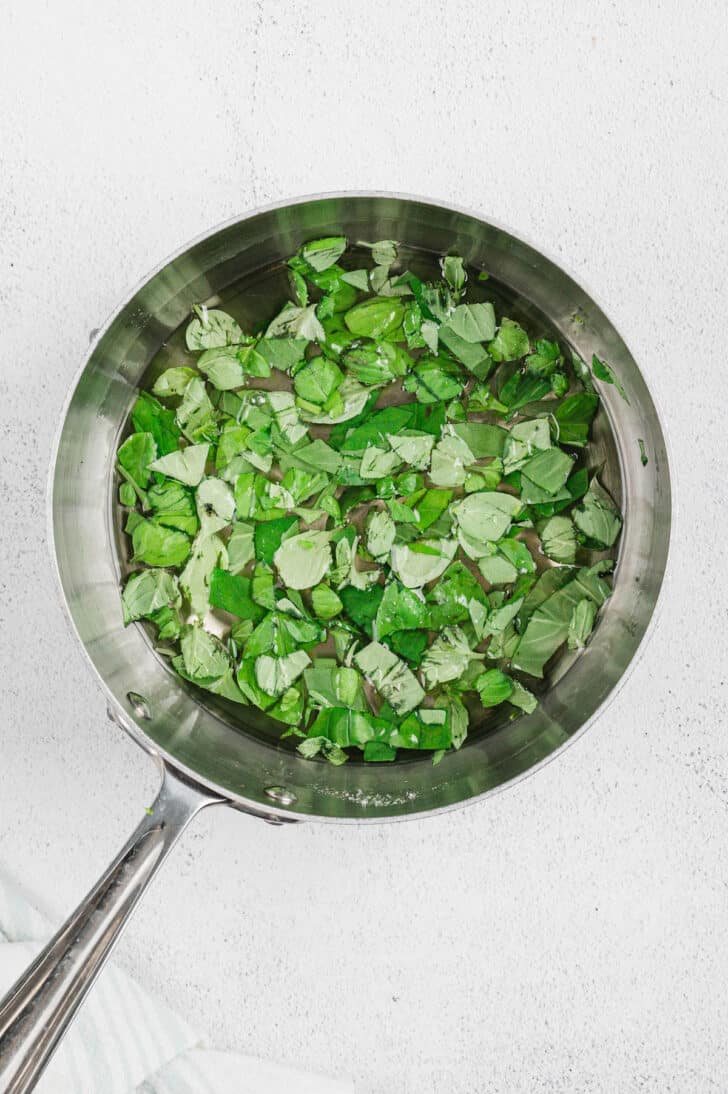 A saucepot filled with clear syrup and chopped green leaves.