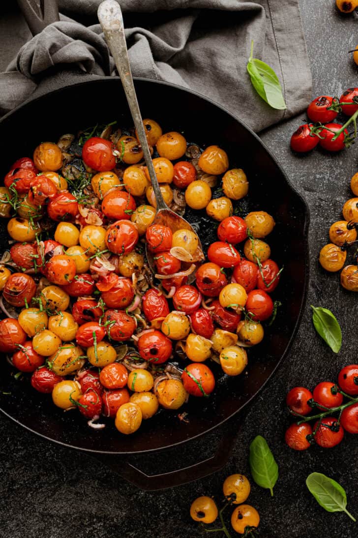 Large cast iron skillet filled with blistered tomatoes, shallots and basil.