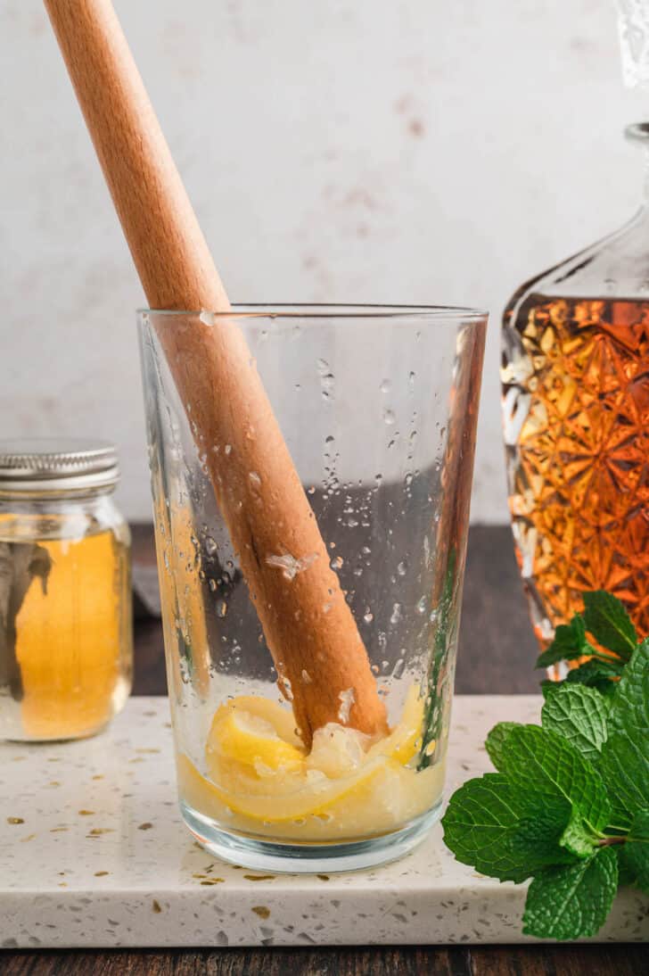 A wooden muddler crushing lemon slices in a tall glass.