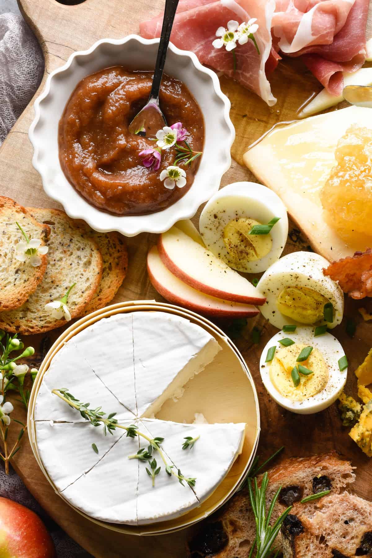 European breakfast items like cheese, eggs, apples and bread, on a wooden board.