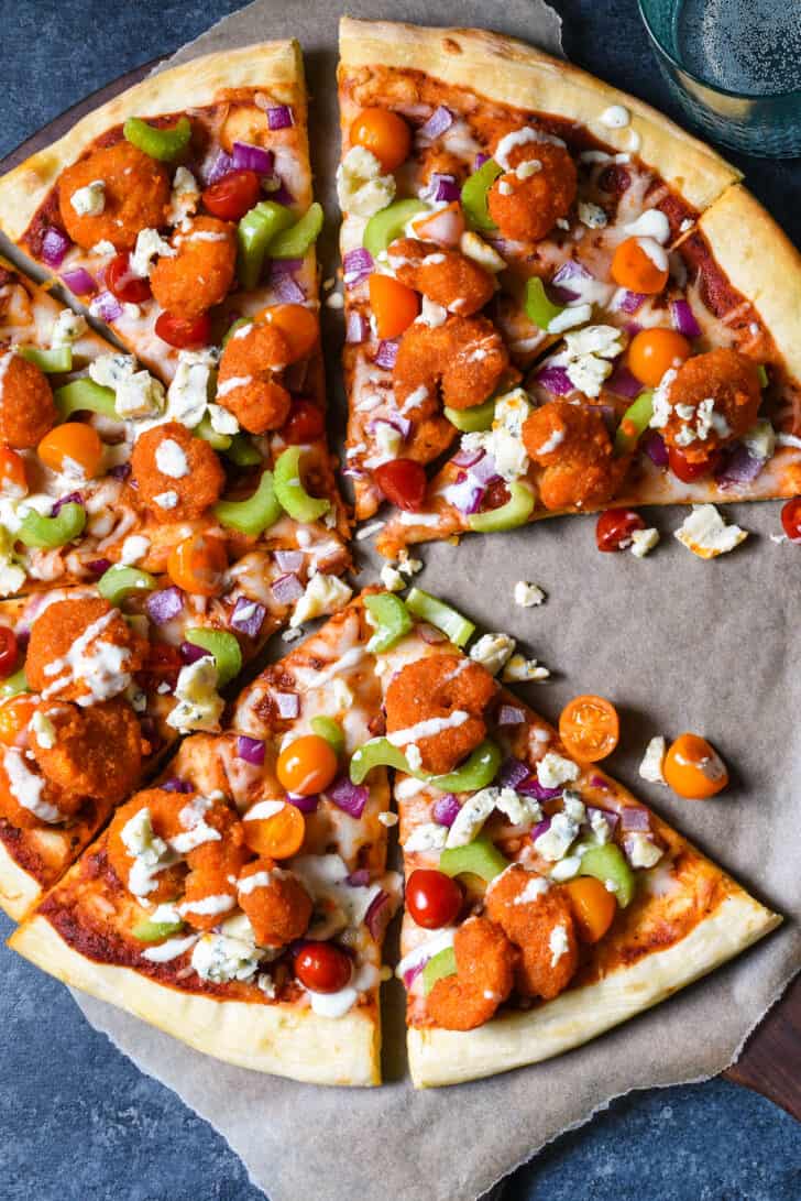 Buffalo shrimp pizza garnished with vegetables, blue cheese and ranch dressing, on brown parchment paper.