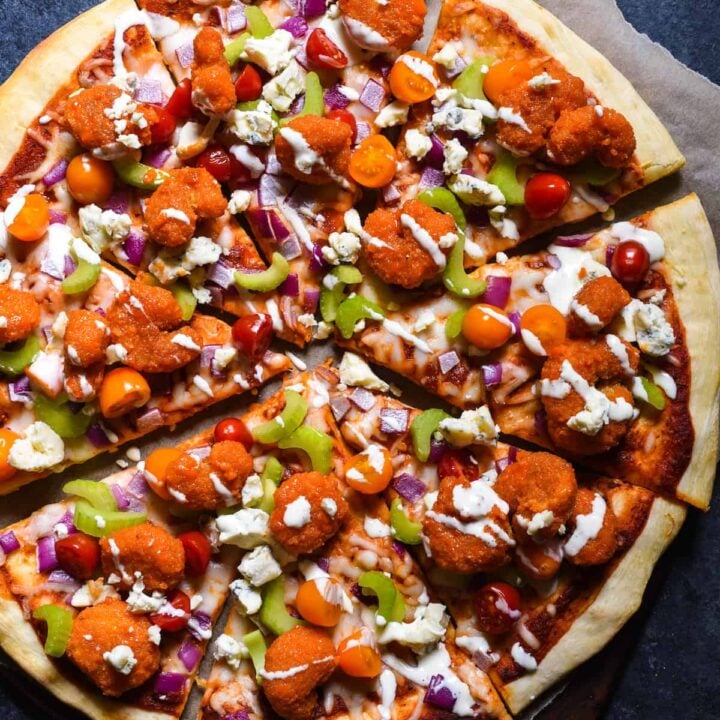 Buffalo shrimp pizza garnished with vegetables, blue cheese and ranch dressing.