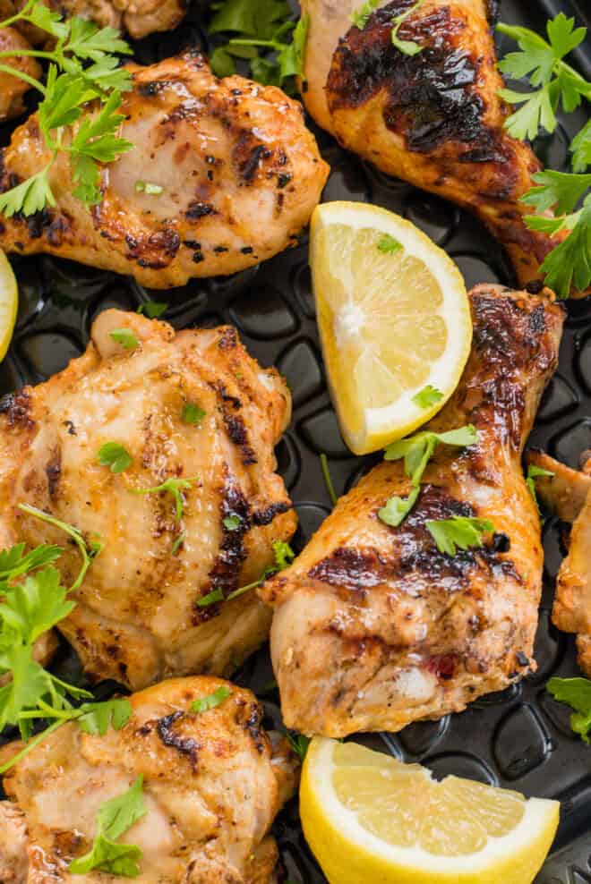 Grilled chicken legs and thighs garnished with lemon wedges and parsley.