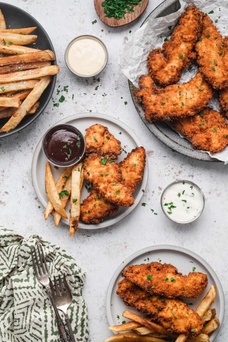 Buttermilk fried chicken tenders and French fries on a small plate with barbecue sauce.