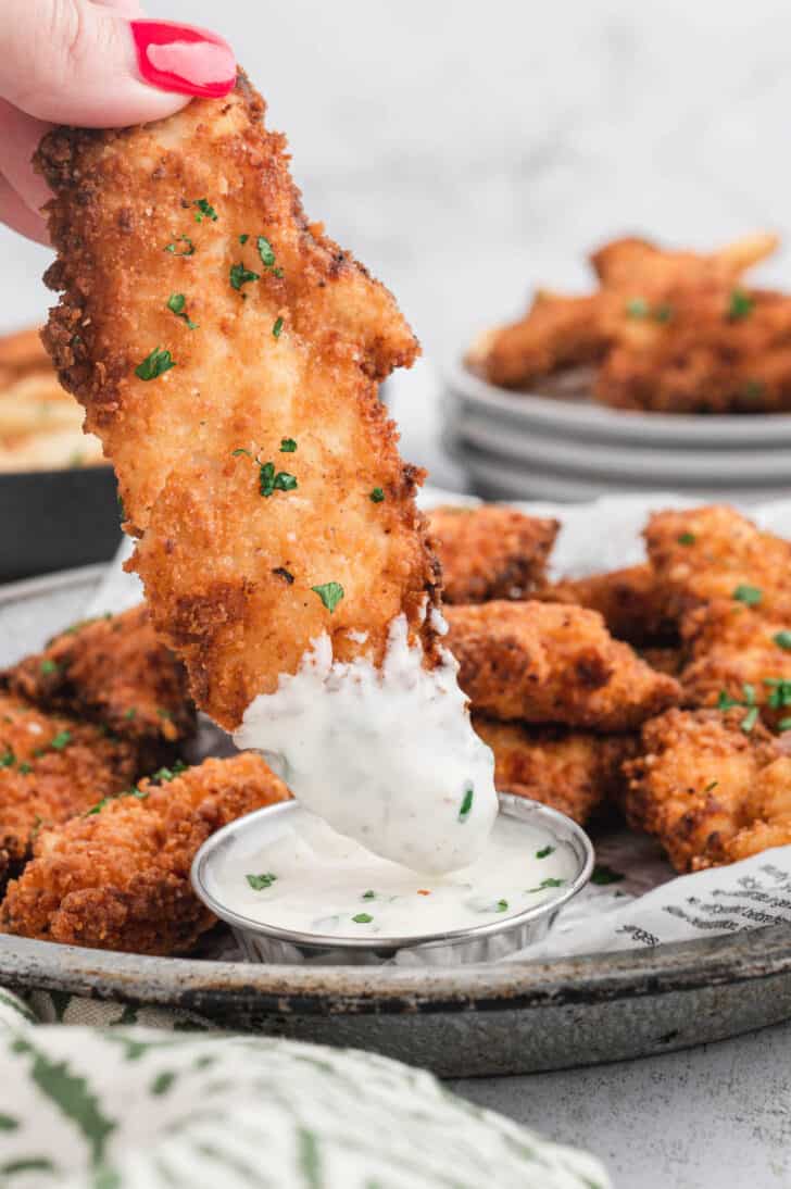 A buttermilk fried chicken tender being dipped into ranch dressing.