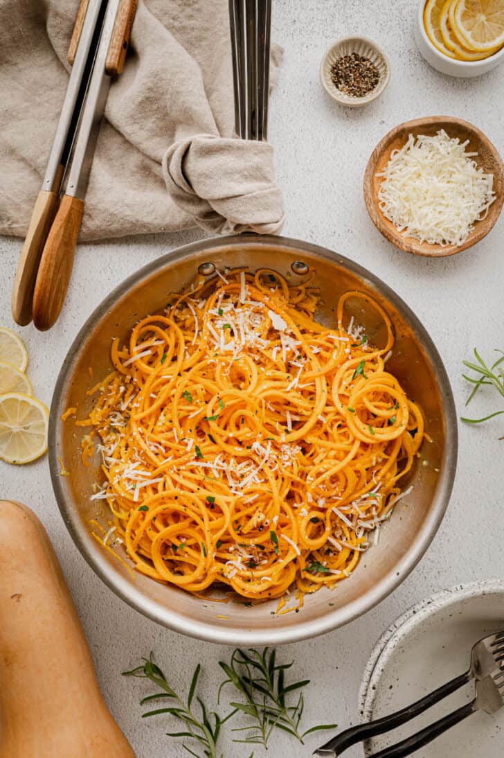 A skillet filled with spirals of orange autumn gourd garnished with herbs and cheese.