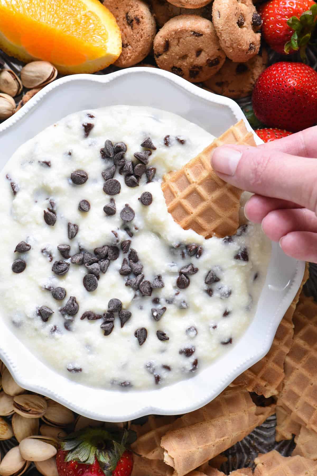 Closeup shot of hand dipping waffle cone piece into creamy dessert dip topped with mini chocolate chips.