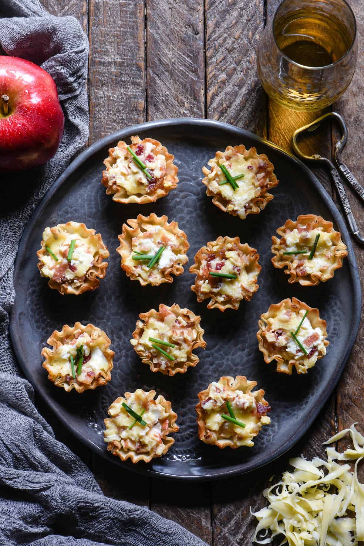 Round gray decorative plate filled with phyllo cup appetizers on a wood table.