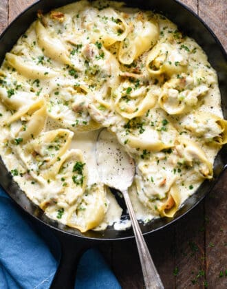 A cast iron skillet filled with chicken alfredo stuffed shells, with a spoon scooping some sauce out.