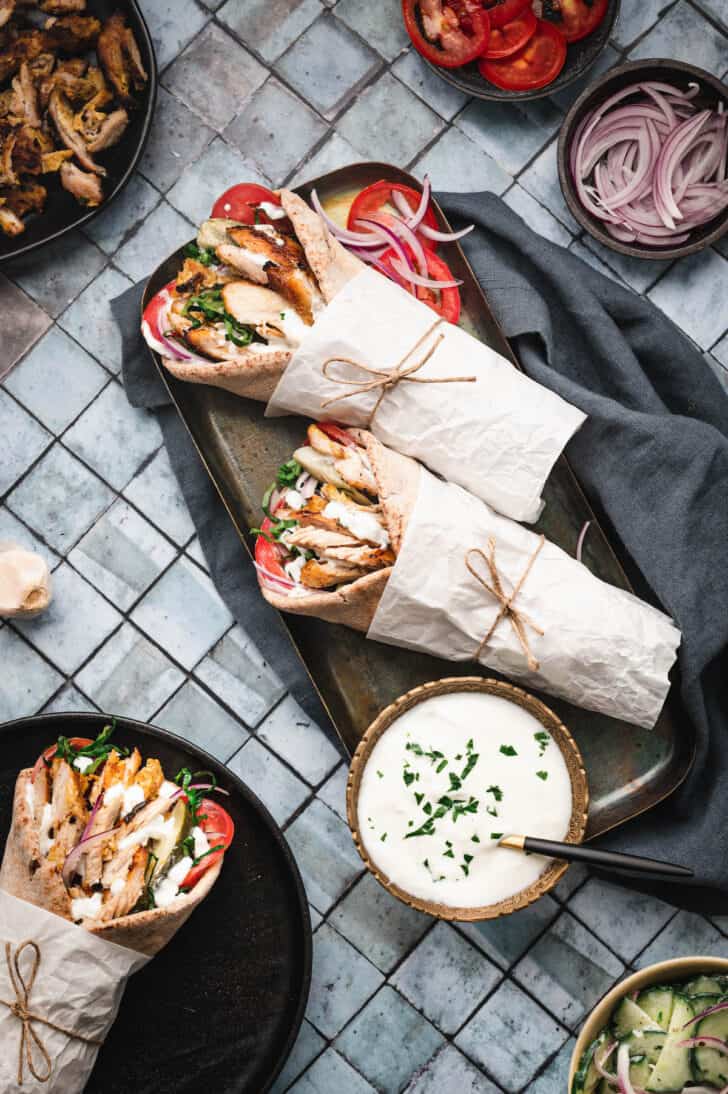 Two chicken shawarma wrap sandwiches wrapped in paper on a metallic tray.