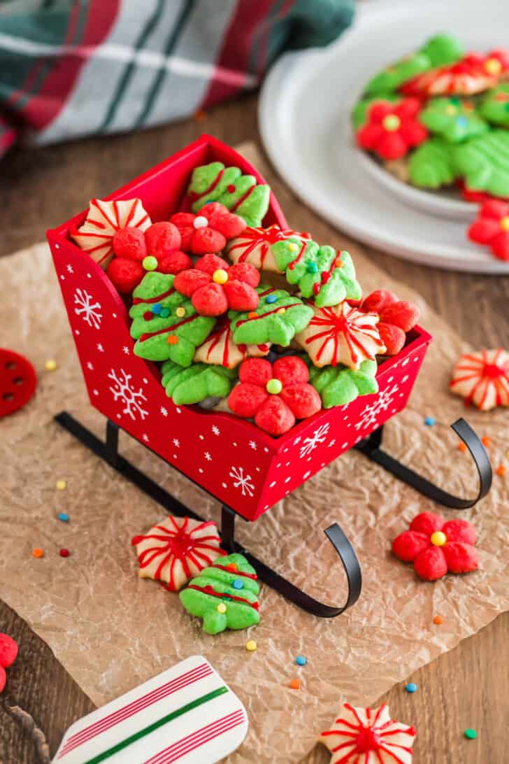 The results of a spritz cookie recipe - red, green and white spritz cookies decorated for Christmas - in a small red decorative sled.