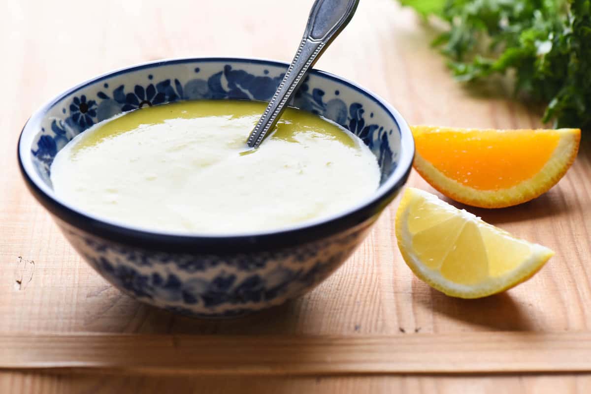 A small painted blue bowl filled with citrus salad dressing with a spoon in it, with orange and lemon wedges nearby.