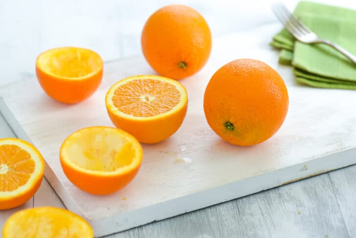 Whole and halved oranges on a white cutting board.