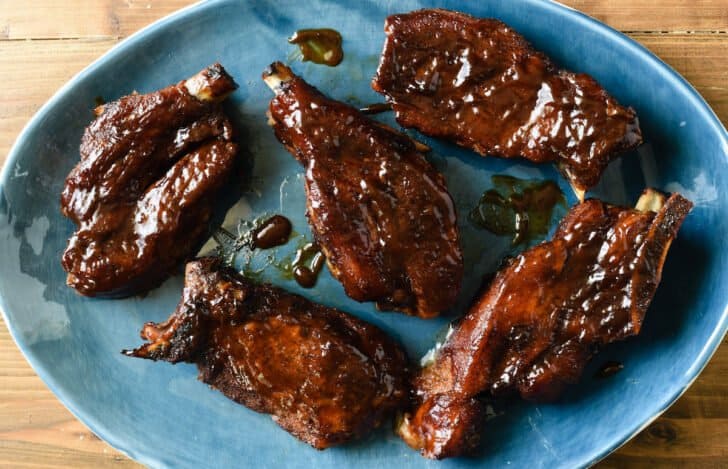 Country style pork ribs glazed with barbecue sauce on an oval shaped blue platter.