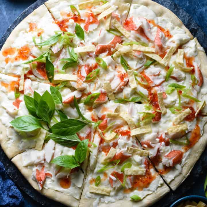 Crab pizza topped with sweet chili sauce, Thai basil and wonton strips, on blue background.