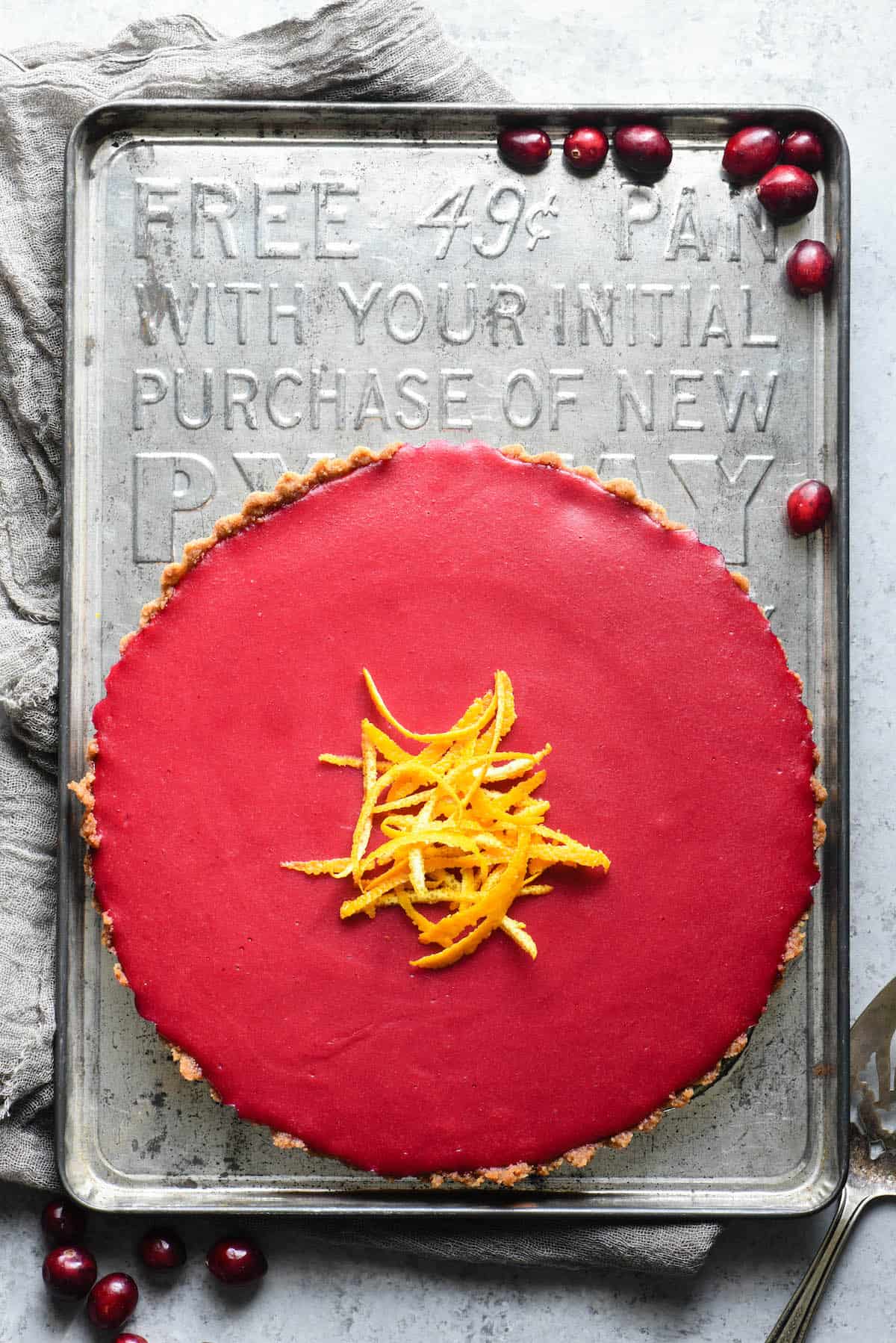 Whole cranberry tart on vintage baking pan, with fresh cranberries scattered around.