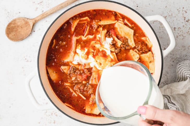 Heavy cream being added to easy lasagna soup in a white Dutch oven.