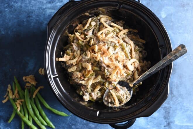 Overhead view of black crockpot insert filled with crockpot green bean casserole, on blue background.