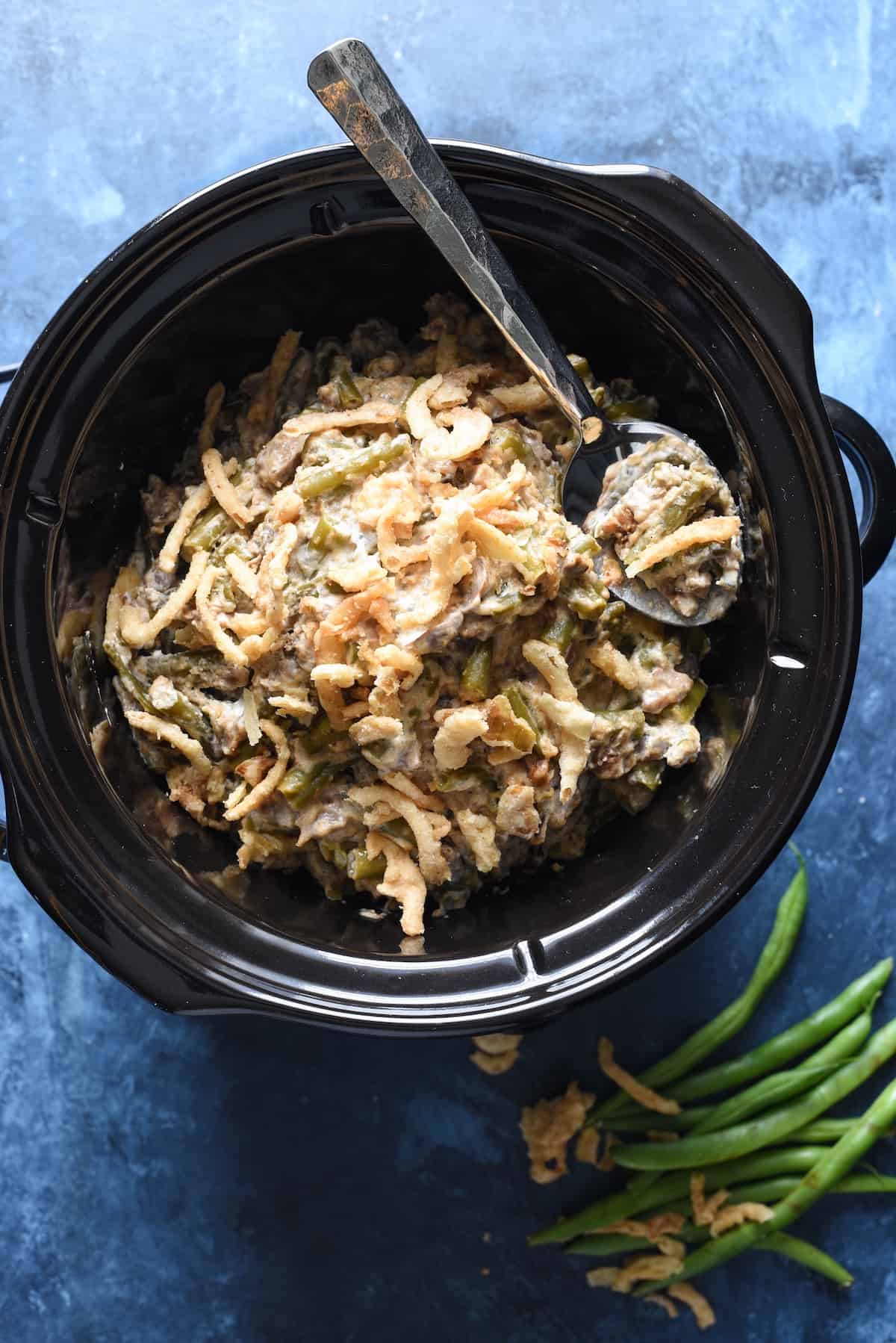 A green bean casserole in crock pot on a blue background.