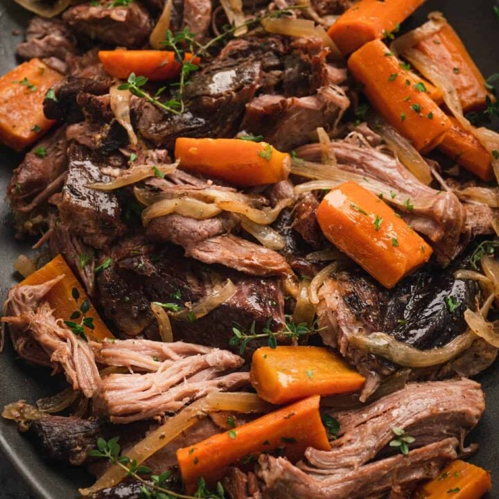 A platter of pork roast crock pot with onions, thyme and carrots.