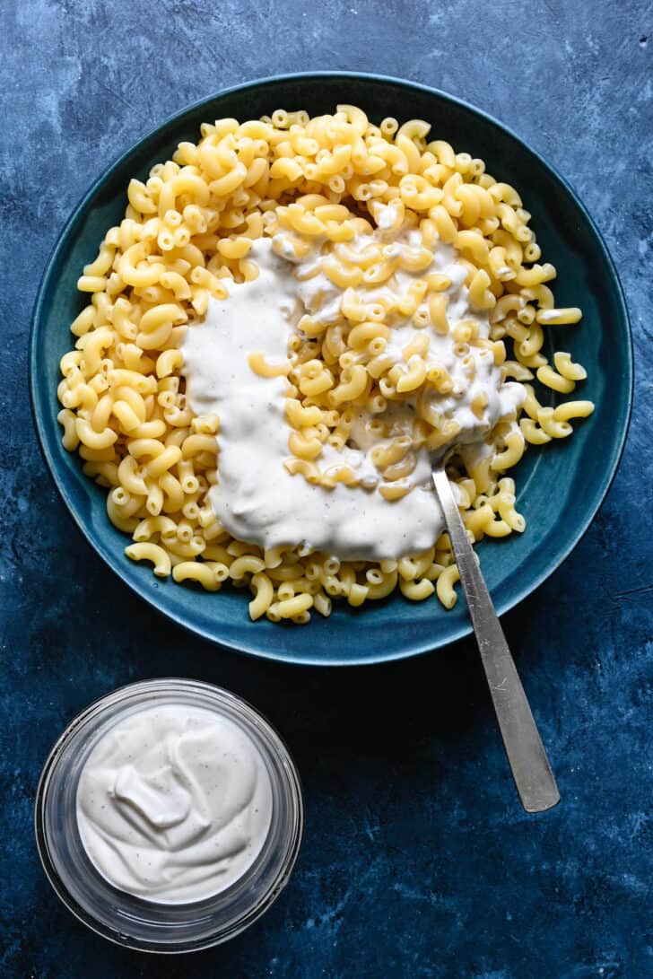 A blue bowl filled with cooked macaroni noodles and creamy sauce, with a spoon stirring it up.