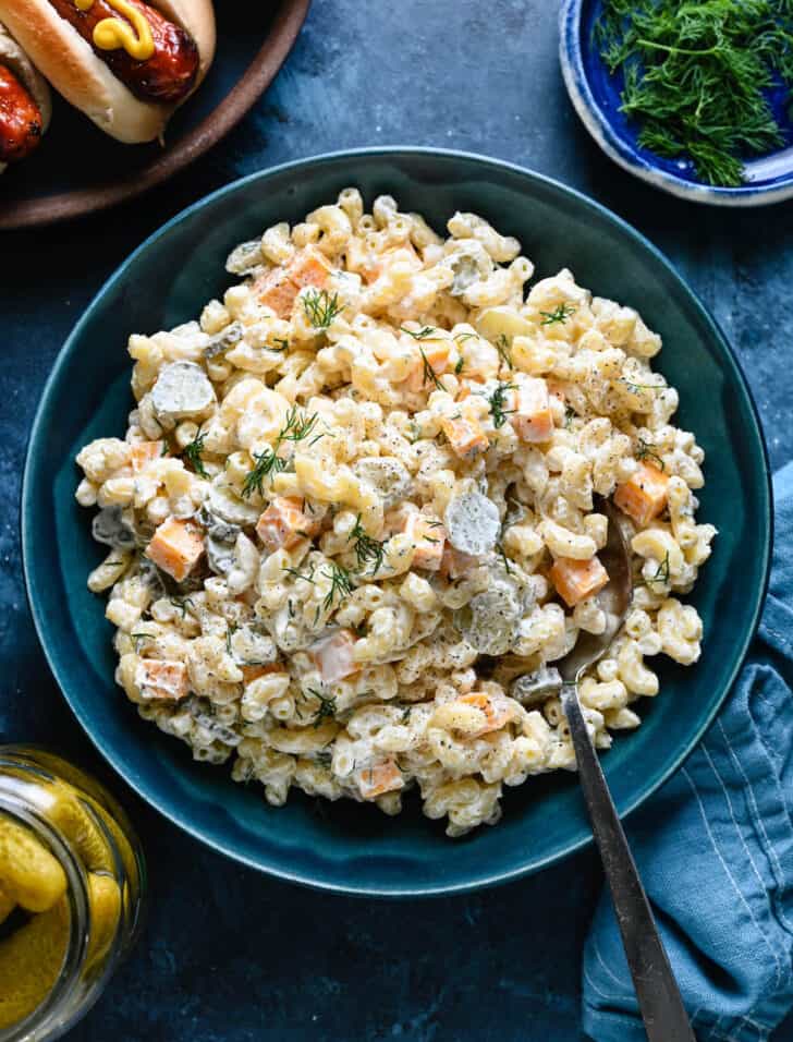 A blue bowl filled with dill pickle pasta salad made with macaroni, fresh dill and cubes of cheddar cheese.