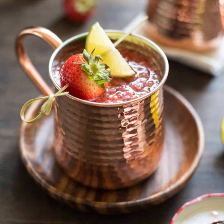 Hammered copper mug filled with strawberry Moscow mule, garnished with a skewer with a strawberry and lime wedge.