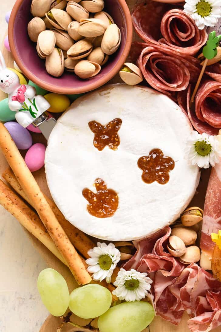 A round of brie cheese with bunny, butterfly and flower shapes cut out of it and filled with orange jam.