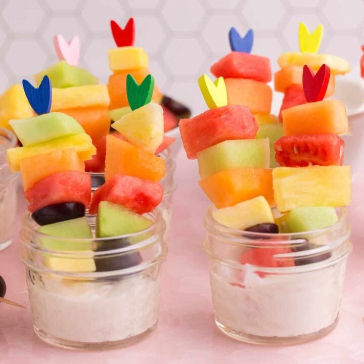 Easter fruit salad, served as half pint mason jars filled with sweet yogurt dip and fresh fruit on fancy toothpicks.