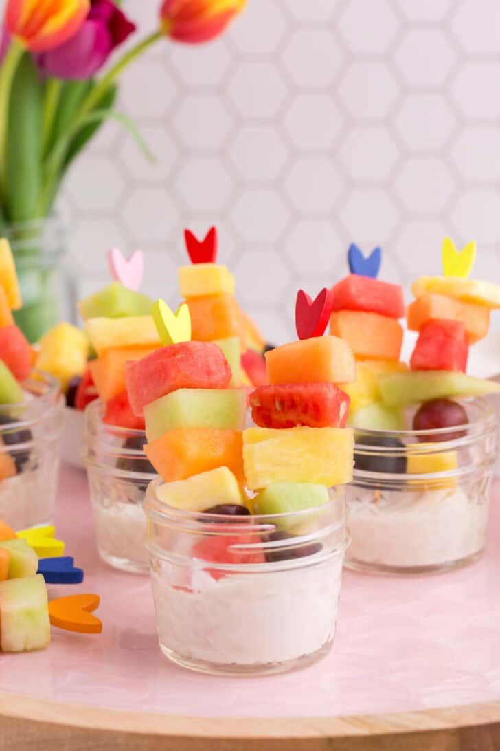 Easter fruit salad, served as half pint mason jars filled with sweet yogurt dip and fresh fruit on fancy toothpicks.