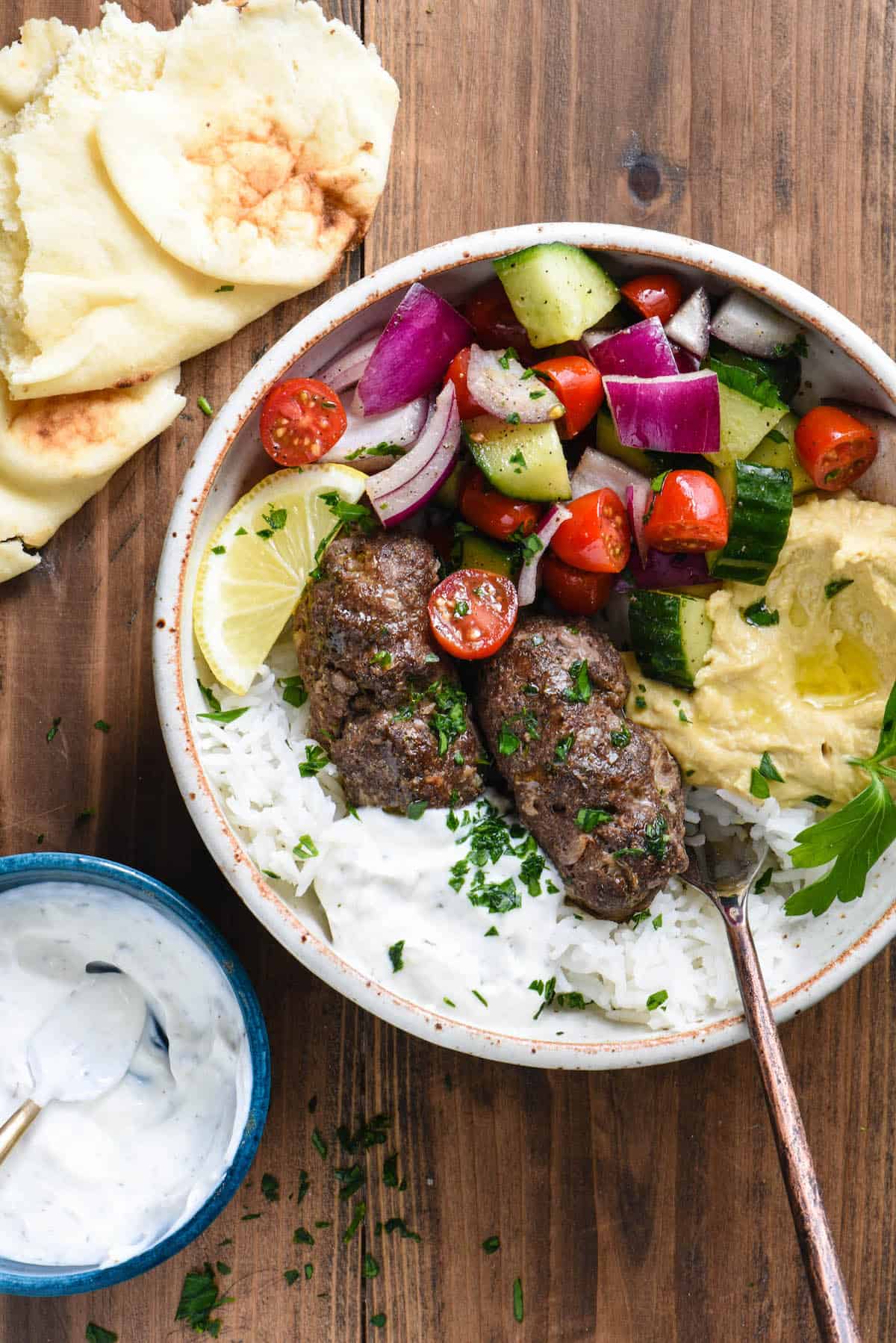 Large bowl filled with rice, kafta, yogurt sauce, hummus and chopped vegetables.