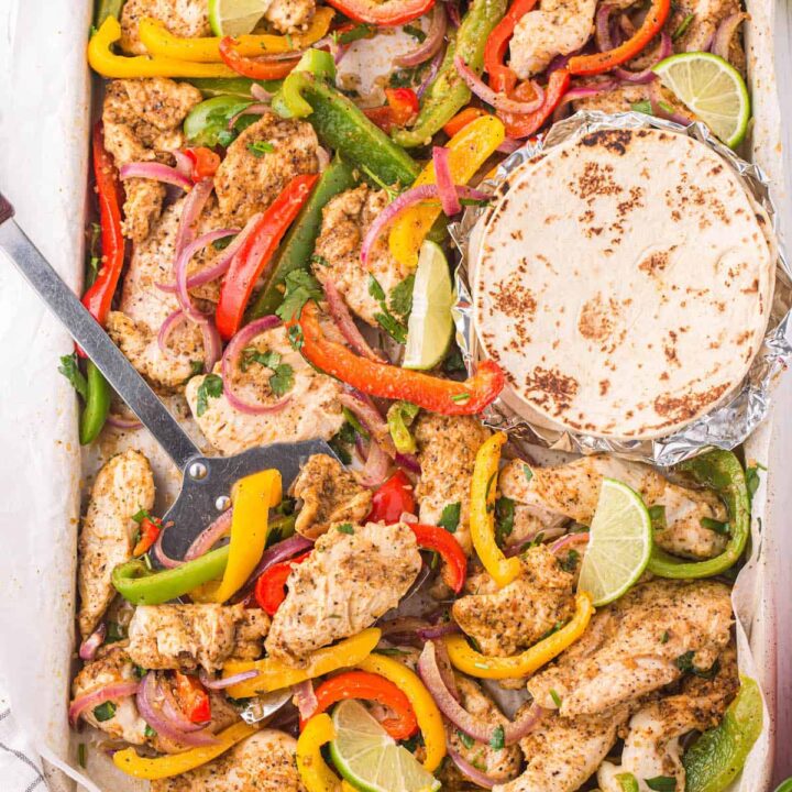 Sheet pan chicken fajitas with flour tortillas, and a metal spatula lifting some of the fajita mixture off the pan.