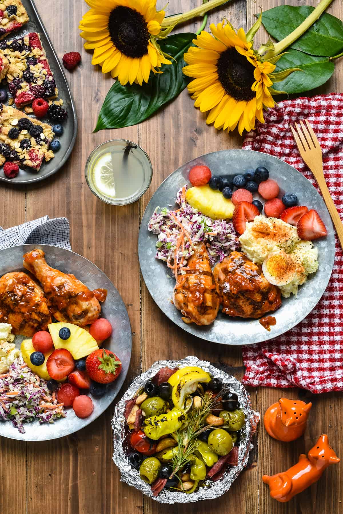 Overhead photo of table covered in plates filled with barbecue food like grilled chicken, coleslaw, potato salad and fruit.