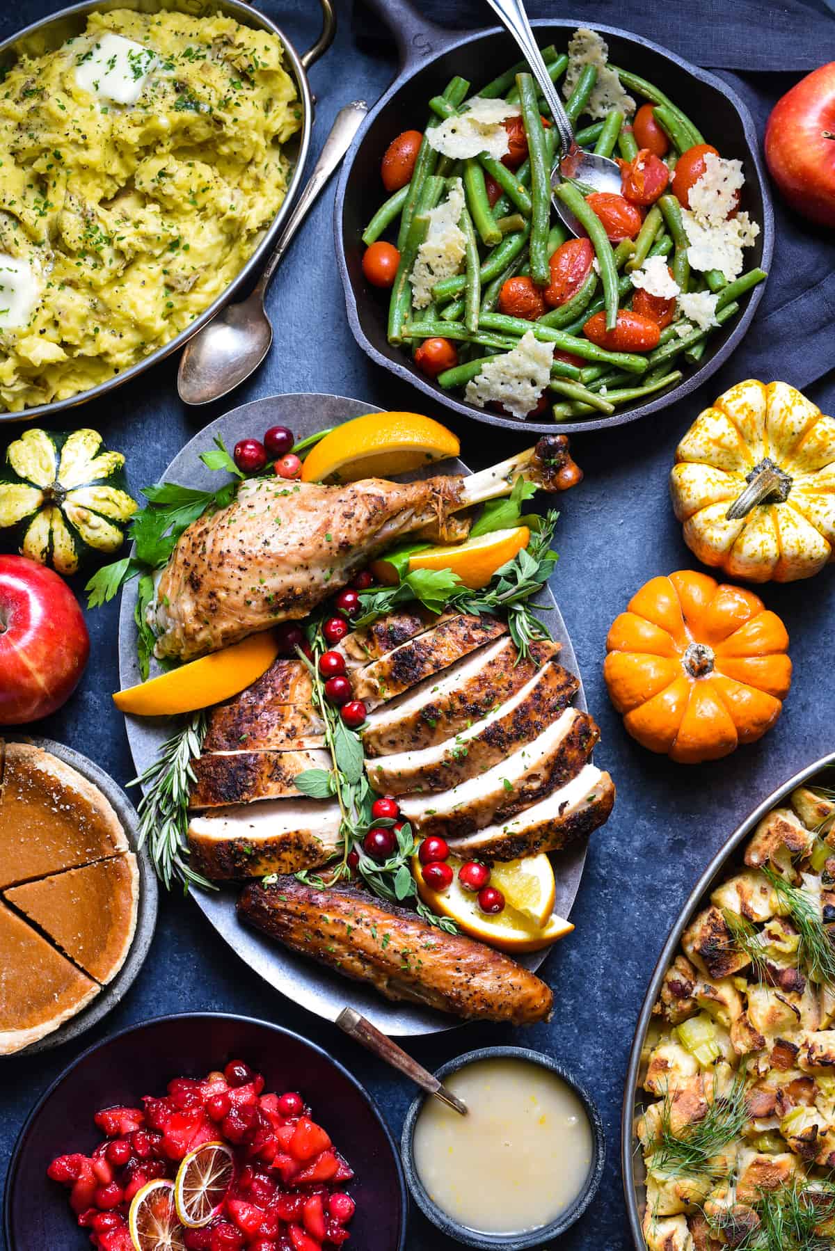 A Thanksgiving feast arranged on a dynamic blue surface, including roasted poultry, mashed potatoes, green beans with tomatoes, cranberry sauce, stuffing and  pumpkin pie.