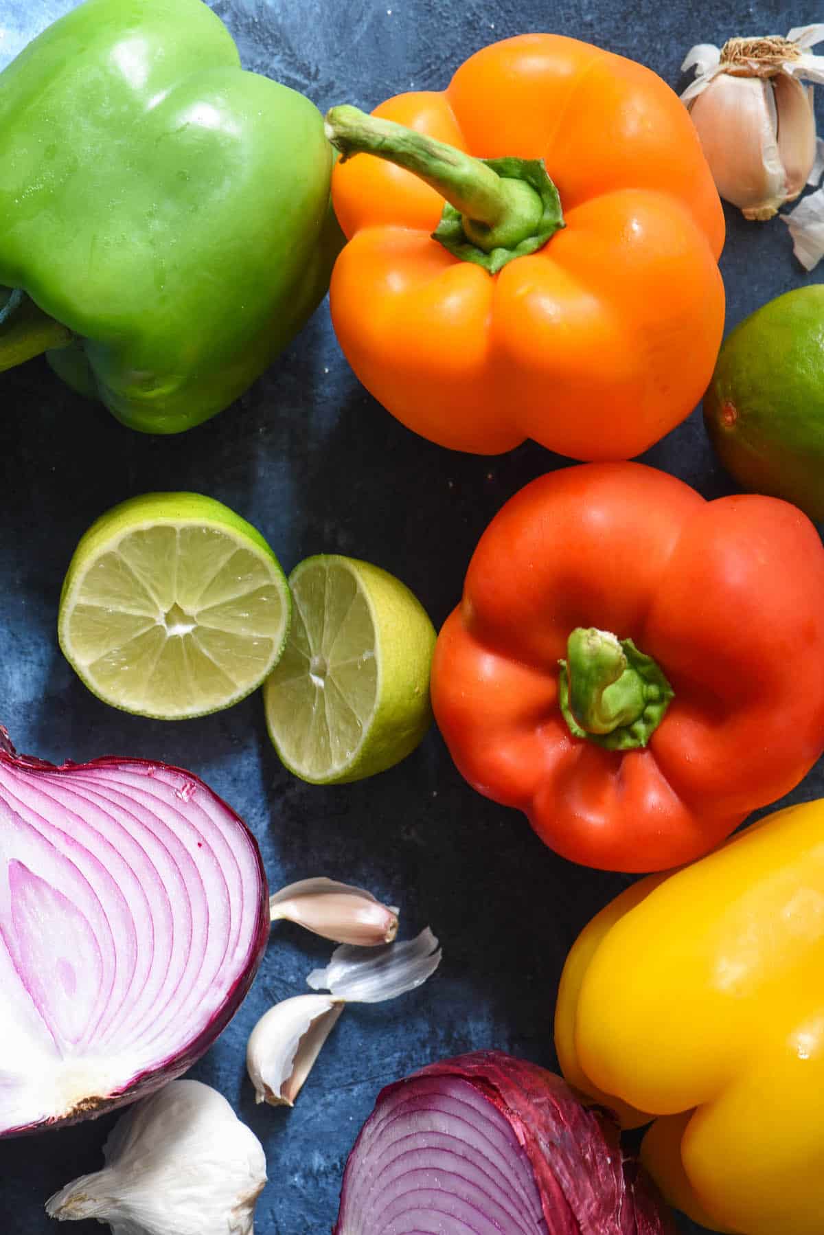 Raw bell peppers, lime, garlic and red onion on blue background.