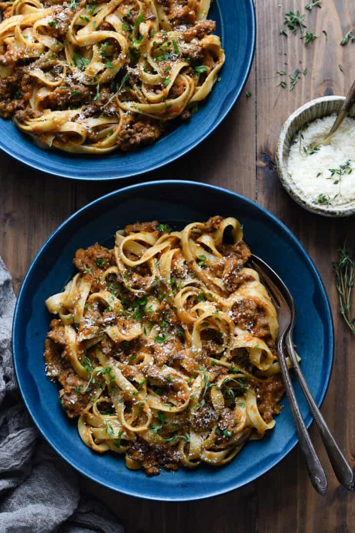 Two blue ceramic bowls filled with fettuccine alla bolognese on a wooden tabletop.