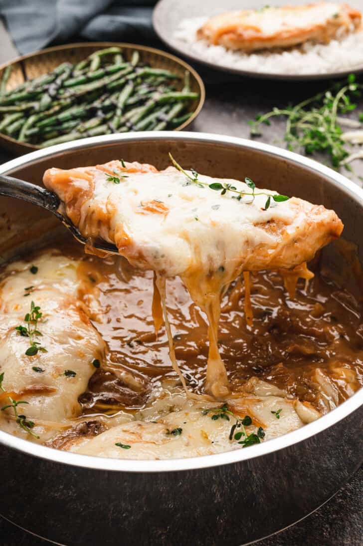 French Onion Chicken being lifted out of a stainless steel skillet.