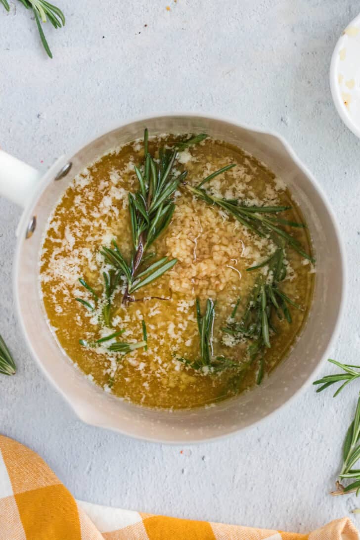 A small saucepan filled with melted butter, minced garlic and rosemary sprigs.